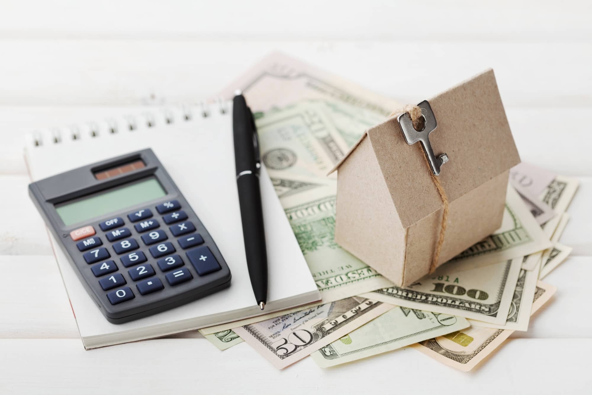 Model of cardboard house with key, calculator, notebook, pen and cash dollars. House building, loan, real estate